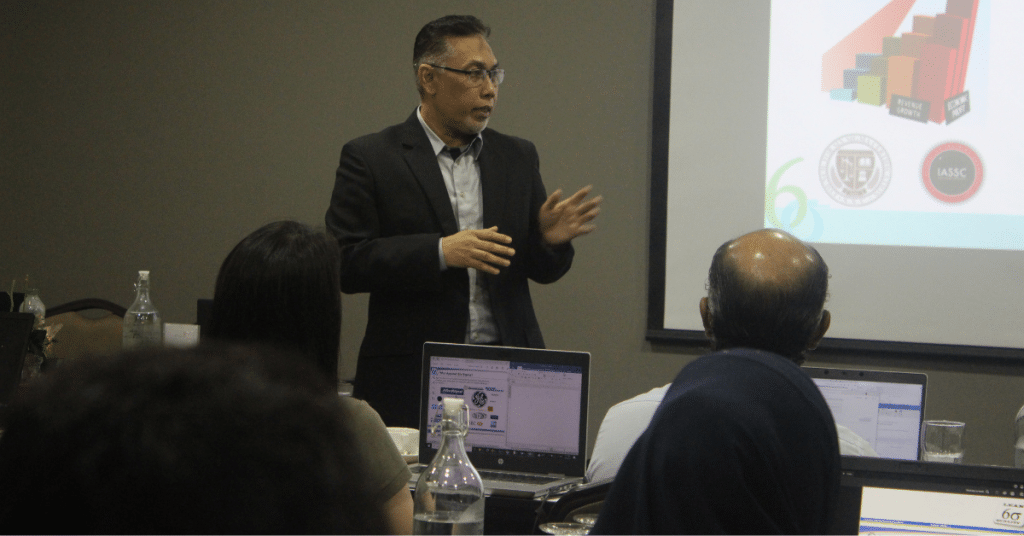 Trainer from MBizM Sdn. Bhd. delivering a presentation on Lean Six Sigma Green Belt concepts during the Program Latihan MADANI at Acappella Suite Hotel.