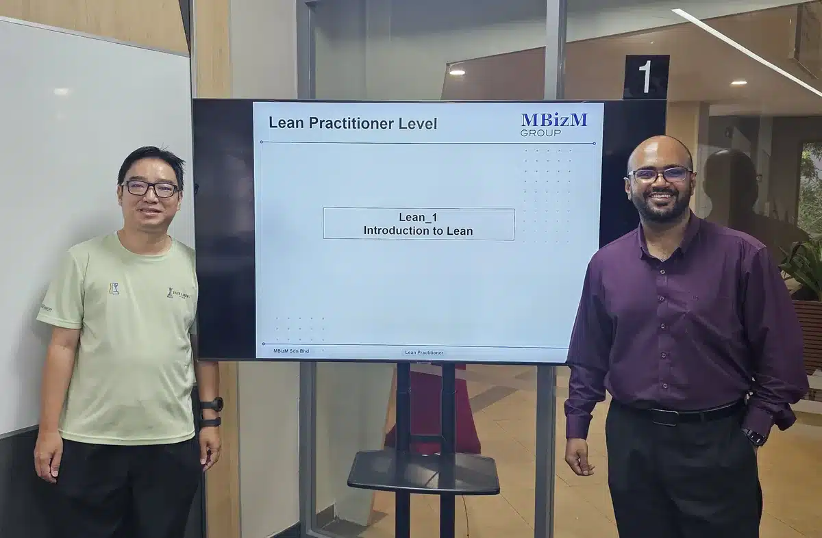The workshop coordinator from Monash University Malaysia and the MBizM trainer beside the Lean Practitioner Level opening slide, Introduction to Lean