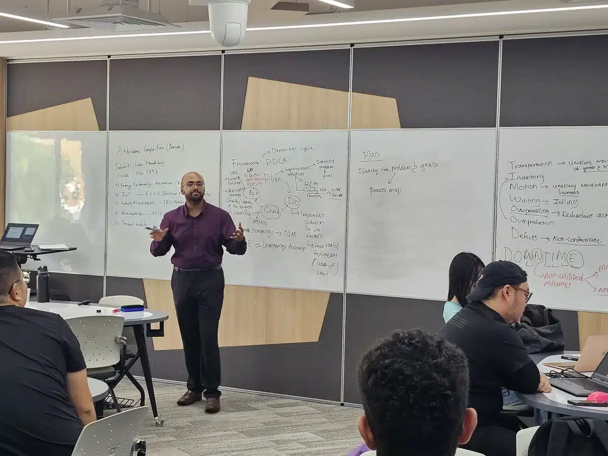 MBizM trainer explaining the PDCA cycle and the eight wastes on the whiteboards to Monash University Malaysia students